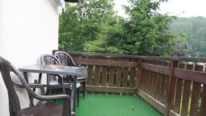 Un espace patio aménagé avec une table et des chaises, entouré d’une clôture en bois et d’une pelouse artificielle verte.