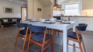 A modern kitchen with white cabinets, a black countertop, and a dining area with a white table and dark chairs. - Comfortable Holiday Apartment in St. Peter Ording (St. Peter-Ording)