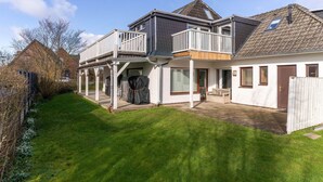 A two-story house with a covered patio, a fenced backyard, and a clear sky. - Comfortable Holiday Apartment in St. Peter Ording (St. Peter-Ording)