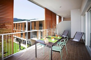 A balcony with a dining table set for two, surrounded by chairs, overlooking a building and a grassy area. - Residence Olivo, Garda (Garda)