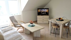 A cozy living room with a sofa, a dining table with chairs, a TV, and a small table with a bowl of fruit. - Apartment <<morskie Oko B>> in Miedzyzdroje (Miedzyzdroje)