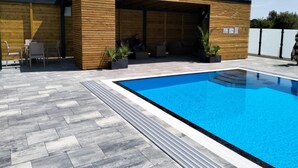 Uma área de piscina moderna ao ar livre, com um deck de madeira e um espaço de estar coberto.