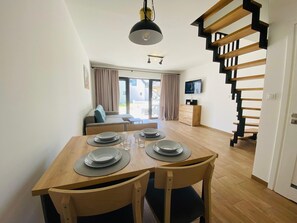 Un coin repas avec une table en bois dressée pour quatre personnes, un canapé et un téléviseur en arrière-plan.
