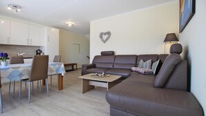A modern living room with a brown leather sofa, a dining table with chairs, and a kitchen area in the background. - Reihenhaus in Plau am See mit Terrasse und Balkon (Plau am See)
