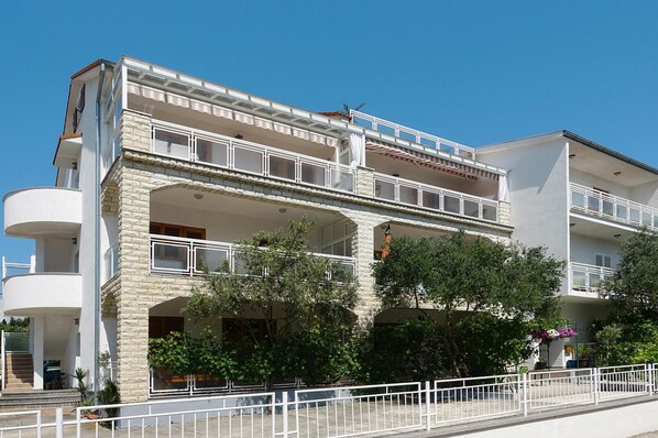 A multi-story building with balconies, a stone facade, and a white railing. - Biograd Beachside Family Apartment (Biograd na Moru)