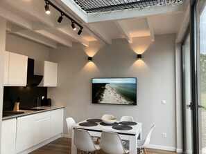 Una cocina moderna con armarios blancos, una mesa de comedor con individuales negros y un televisor de pantalla plana grande montado en la pared.