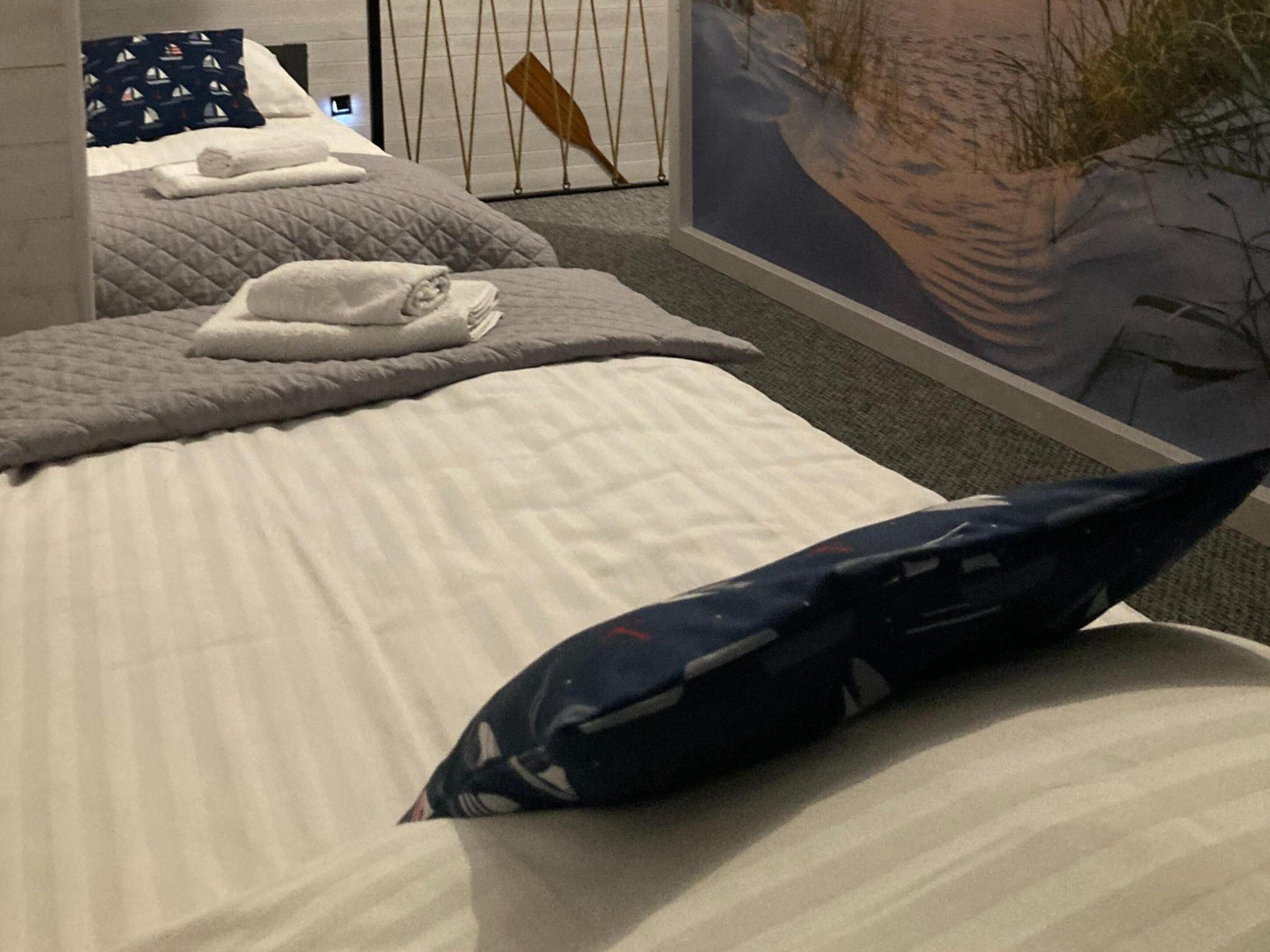 A hotel room with a bed, pillows, a wall-mounted TV, and a potted plant.