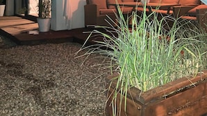 Una casa moderna con un amplio ventanal, una terraza de madera y un rincón de descanso con cojines.