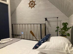 Ein Schlafzimmer mit einem Bett, einem an der Wand befestigten Schiffswalzenrad, einer hängenden Rettungsleine und einem Blumentopf.