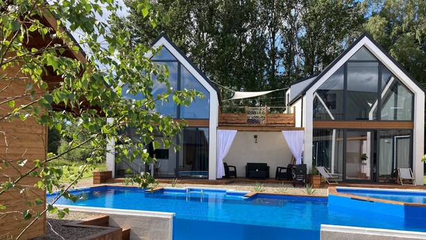 Un área de piscina moderna con dos edificios adyacentes, una piscina azul cristalina y mobiliario exterior.