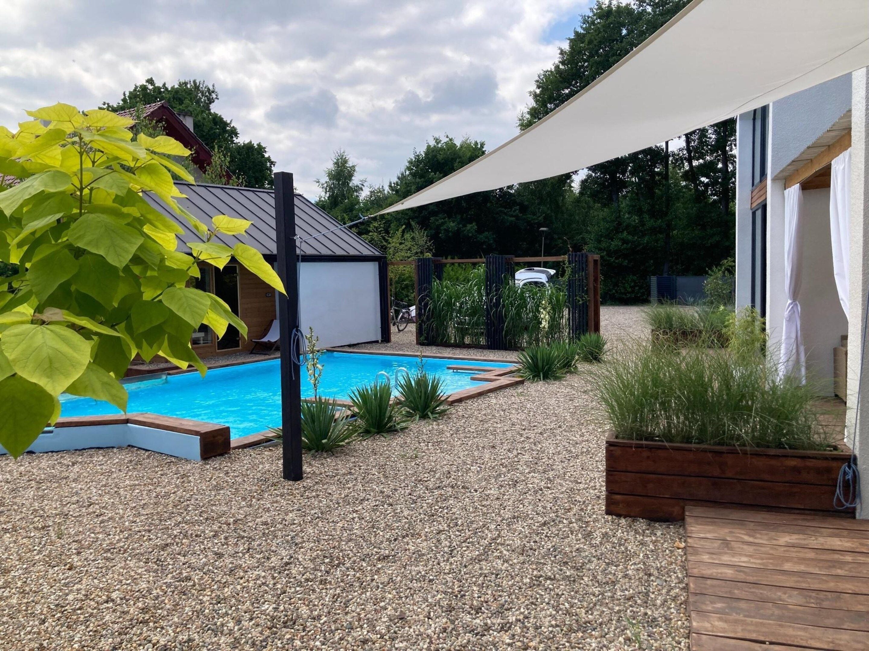 Un jardin avec une piscine, une terrasse en bois et un espace salon abrité.