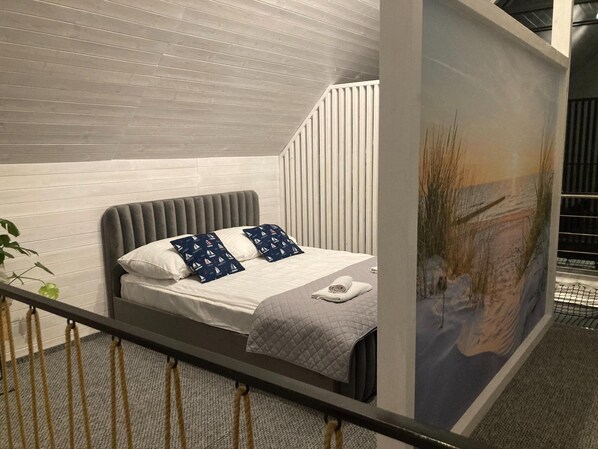 A modern bedroom with a bed, pillows, a quilted blanket, and a view of a cityscape through a window.