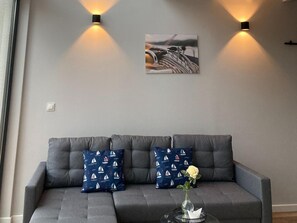 Ein graues Sofa mit zwei gemusterten Kissen und einer Vase mit einer einzelnen Blume auf einem Beistelltisch.