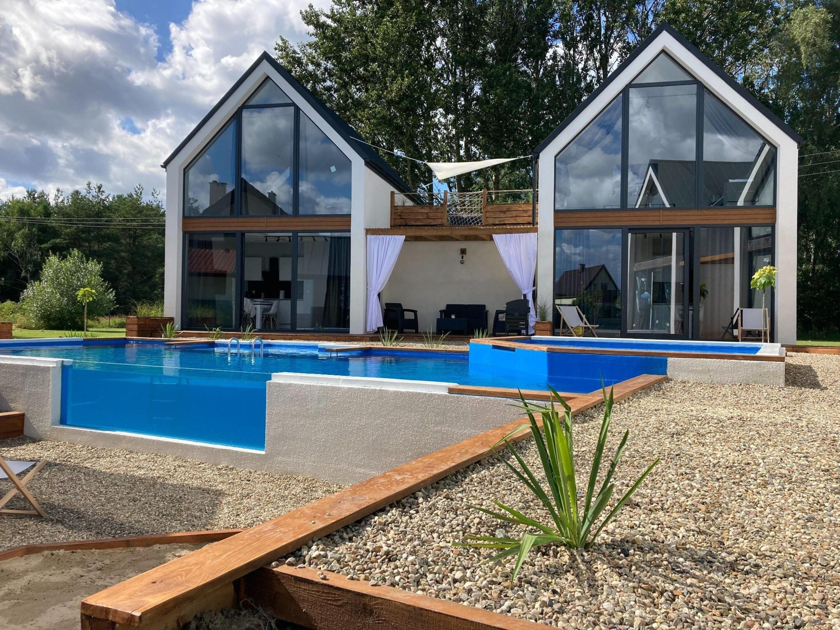 A modern two-story house with a swimming pool, wooden deck, and outdoor furniture.