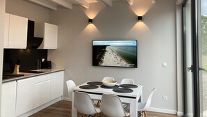 Una cocina moderna con armarios blancos, una zona de comedor con mesa y sillas, y un ventanal con vistas a la playa.