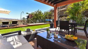 Eine Außenpatio mit einem Glastisch, Korbmöbeln und Blick auf einen Pool und Grünflächen.