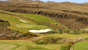 En golfbana med bunkrar, ett vattenhinder och en bergig bakgrund.