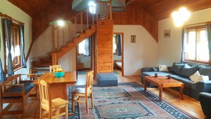A wooden interior with a staircase, a sofa, a dining table with chairs, and a patterned rug. - Apartment in Masuria With Private Pond (Gizycko)