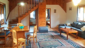 A cozy cabin interior with a wooden staircase, a dining area with a table and chairs, a sofa, and a patterned rug. - Apartment in Masuria With Private Pond (Gizycko)