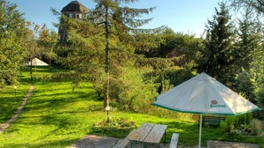 A picnic area with a table and benches, surrounded by lush greenery and a distant building. - Apartment in Masuria With Private Pond (Gizycko)