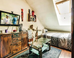 A small, cozy room with a wooden cabinet, a glass coffee table, a bed with patterned bedding, a television, and a wall-mounted shelf with decorative items. - Large Holiday Home by the Lake, Close to the sea (gmina Będzino)