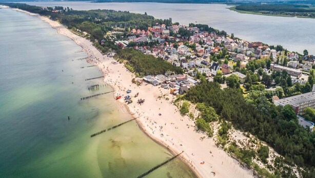 An aerial view of a coastal town with a sandy beach, a pier, and residential buildings. - Large Holiday Home by the Lake, Close to the sea (gmina Będzino)