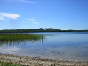 Un lac paisible, avec une plage de sable et une colline boisée en arrière-plan.