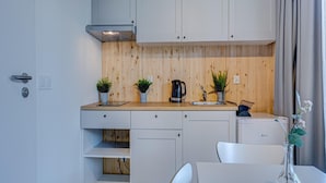 Eine kompakte Küche mit weißen Schränken, einer Holz Arbeitsplatte und einem eingebauten Herd. Auf der Arbeitsplatte befinden sich zwei Blumentöpfe und ein kleines Spülbecken.