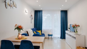A modern living room with a dining area, featuring a sofa, a TV on a white console, and a dining table with chairs. - Apartment in Lukecin Near Baltic Sea (Dziwnów)