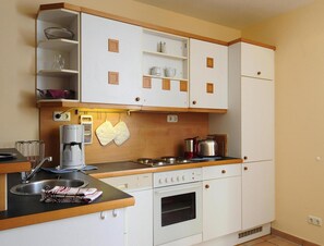 Cuina compacta amb armaris blancs, forn integrat, cafetera i tetera a la superfície.
