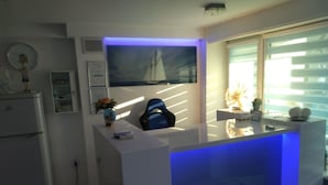 Una moderna reception con illuminazione blu, un'ampia finestra con persiane, un frigorifero e una sveglia a parete.