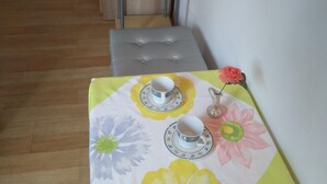 Un tavolino con tovaglia floreale, due tazze, piattini e un fiore rosa.