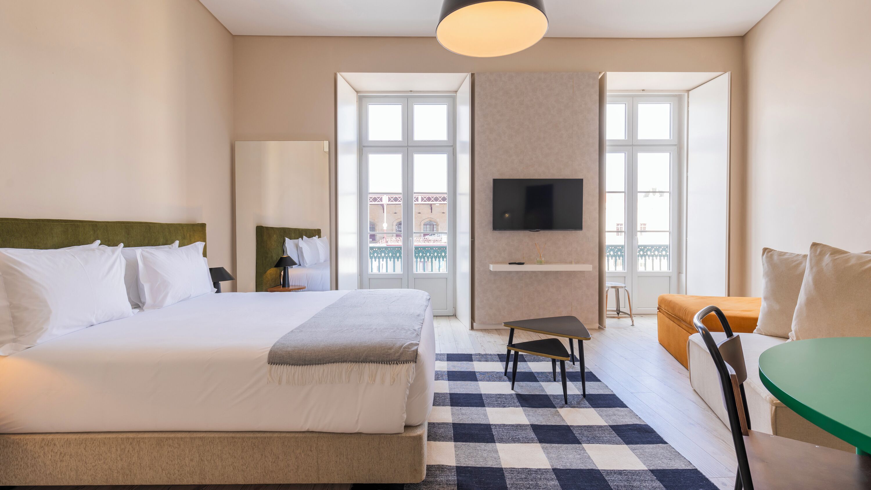 Ett hotellrum med en stor säng, ett skrivbord, en stol, en TV och en balkong med utsikt.
