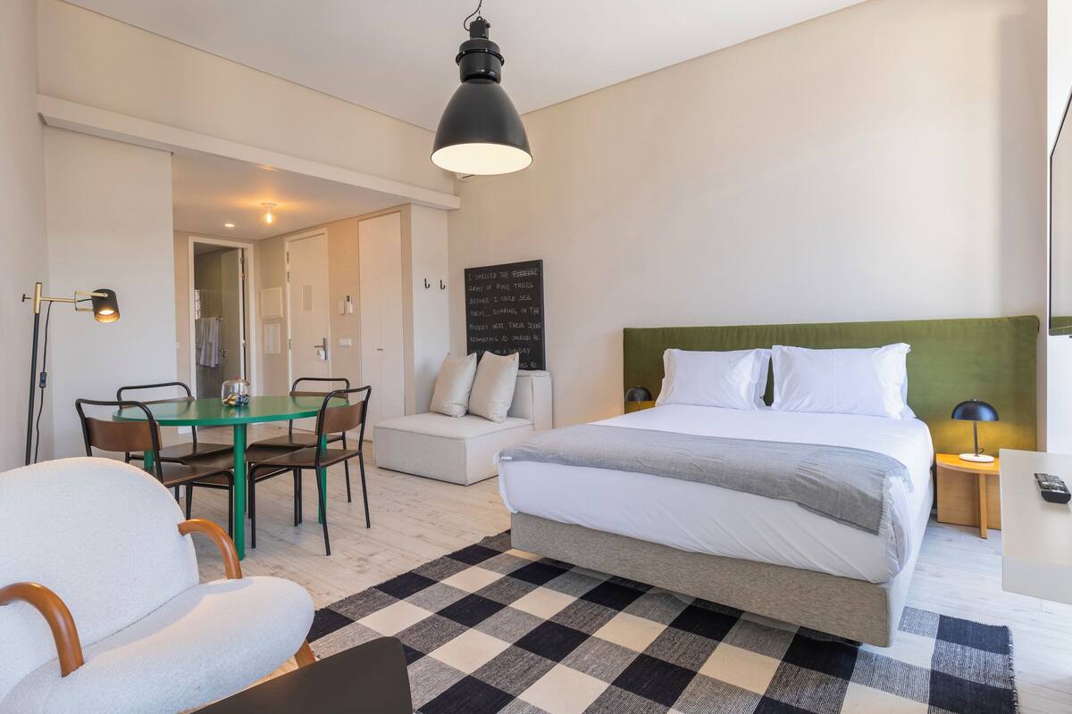 Habitación de hotel con cama, escritorio, silla, mesa de comedor y televisor.