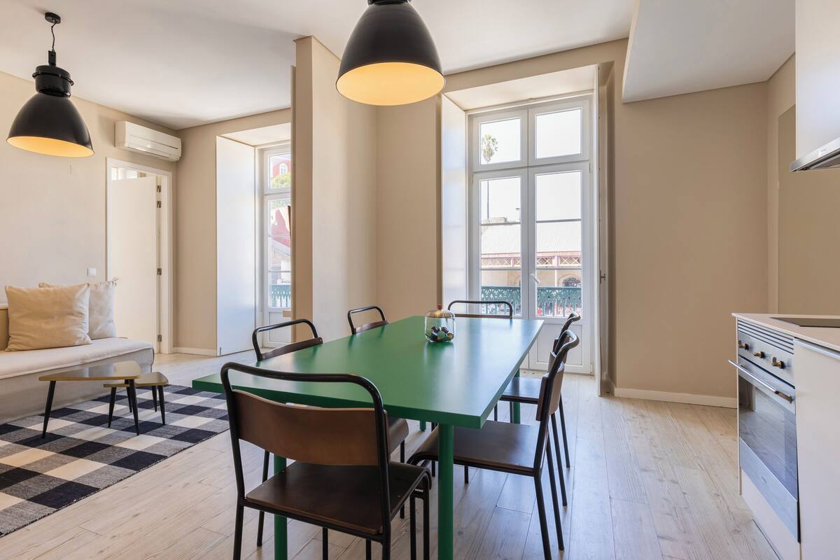 Una cocina moderna con comedor, que incluye una mesa verde, sillas negras e iluminación colgante.