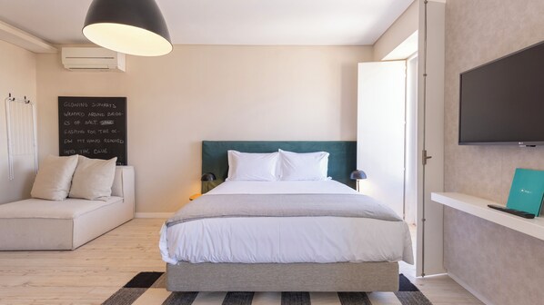 A modern bedroom with a bed, a sofa, a TV, and a chalkboard with text.
