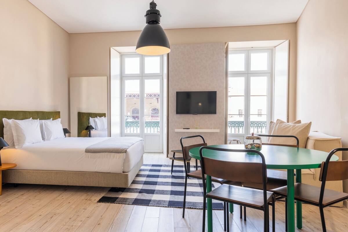 Una habitación de hotel moderna con una cama, un escritorio, un televisor y un balcón con vistas.