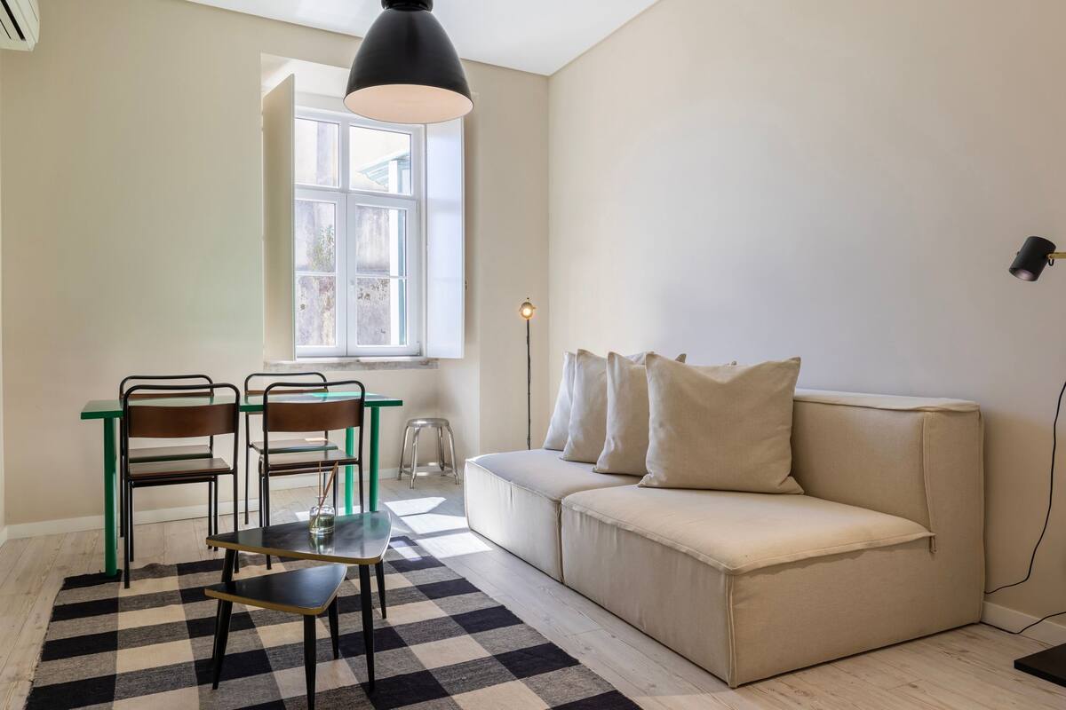 Una habitación con sofá, dos sillones, una mesa, lámpara y ventana.