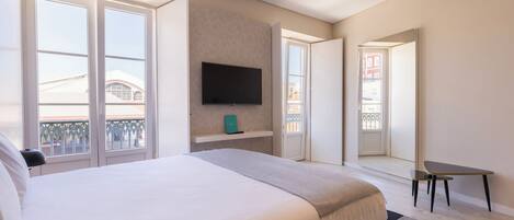 A modern hotel room with a large bed, a flat-screen TV mounted on the wall, and a small table with chairs.