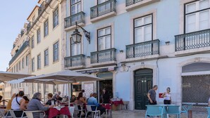 Un café al aire libre con mesas y sillas, un edificio con balcones, y un letrero que dice "OADRANNO".