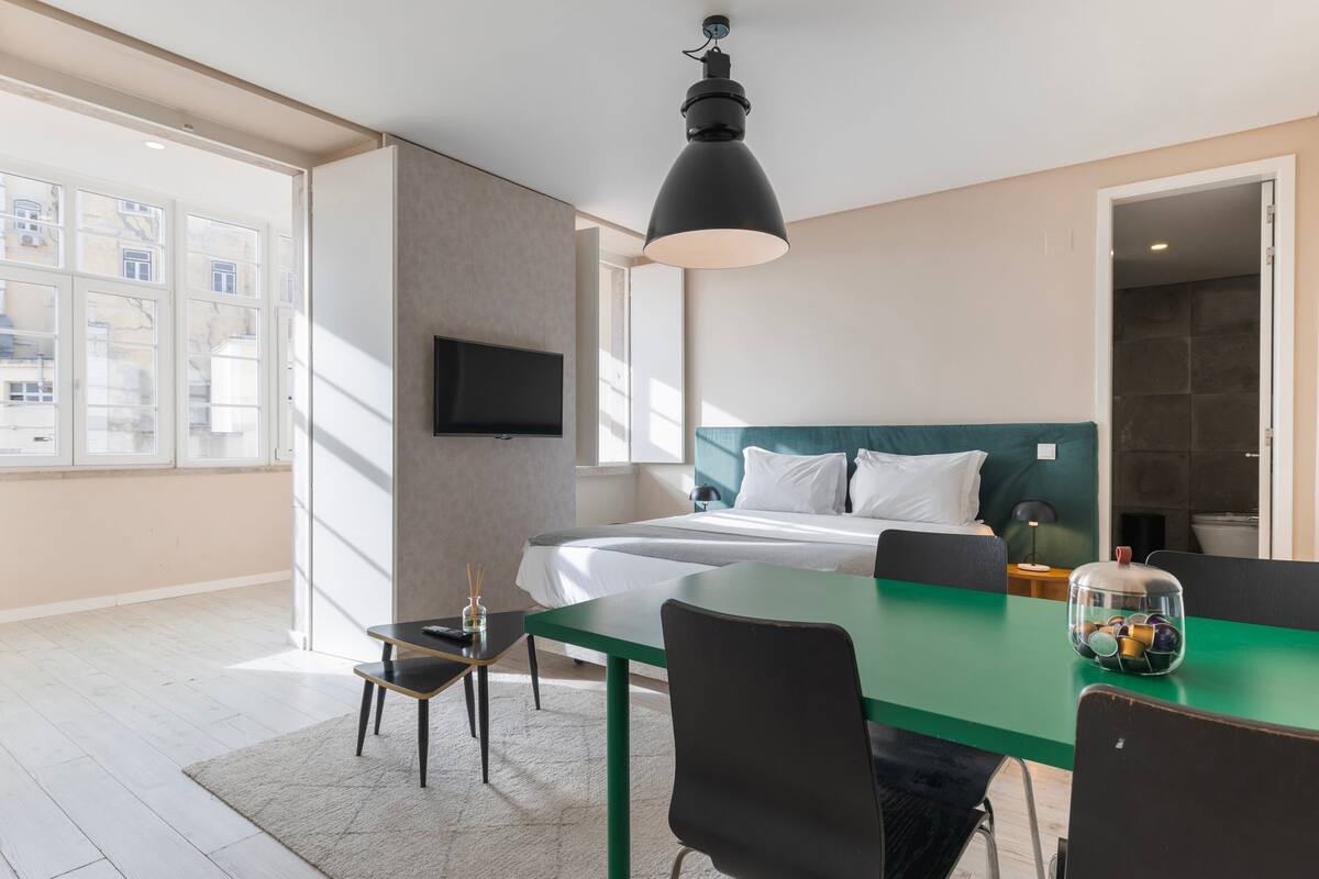 Una habitación de hotel moderna con una cama grande, una mesa de comedor y un televisor montado en la pared.