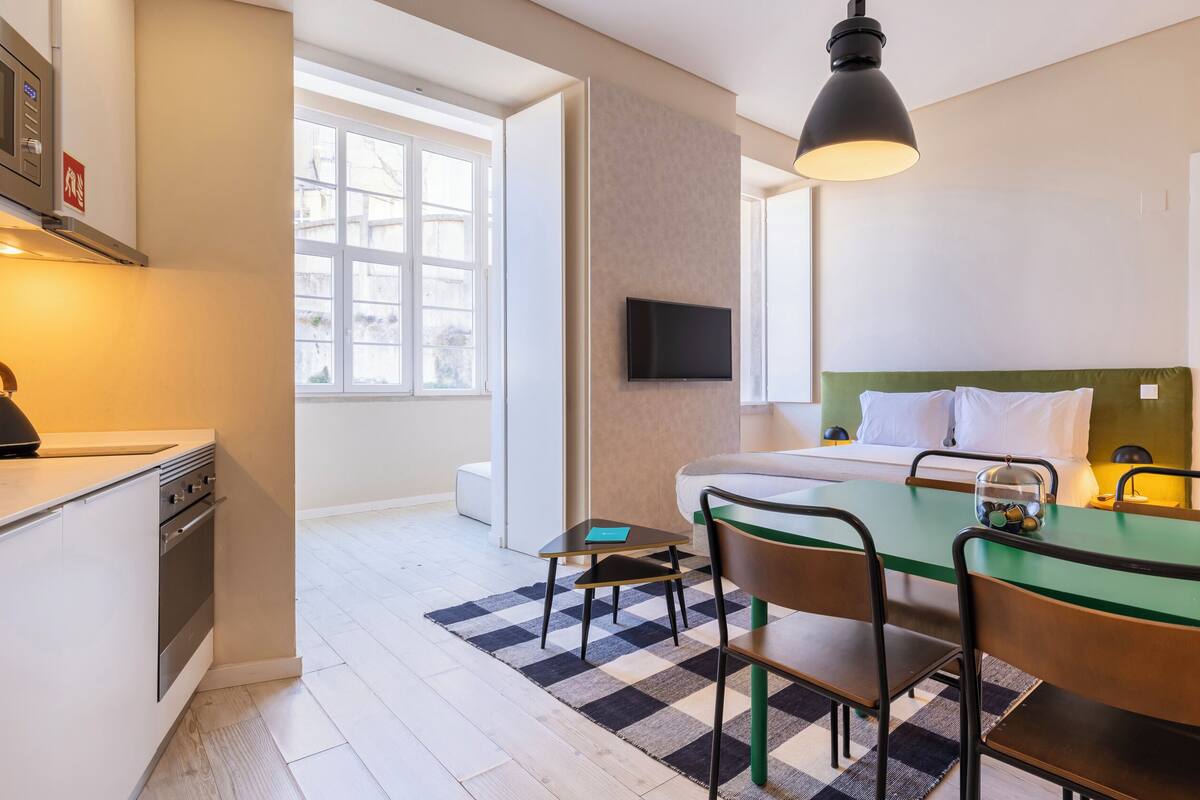 Una habitación de hotel moderna con cama, escritorio, silla, televisor y kitchenette.