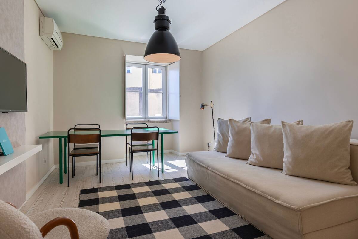 Una sala de estar moderna con un sofá, una mesa de comedor con sillas, un tapete a cuadros blanco y negro, y un ventanal grande.