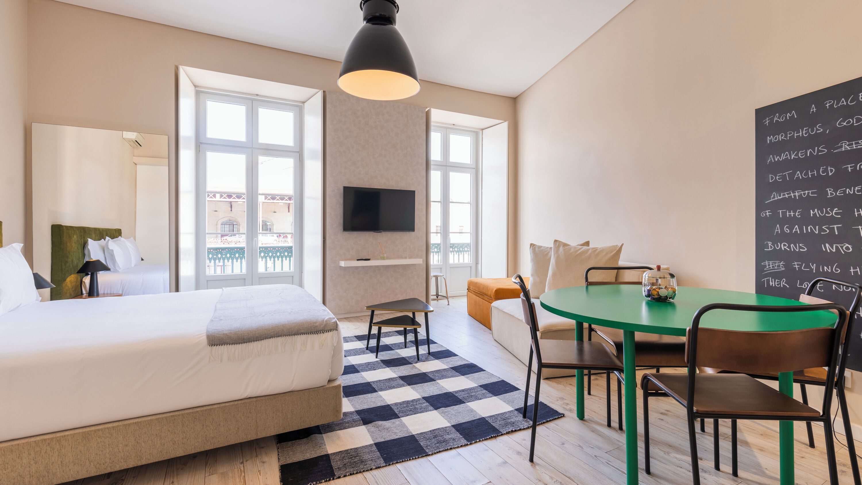 Ein Hotelzimmer mit Bett, Schreibtisch, Stuhl, Tisch, Fernseher und Balkonblick.