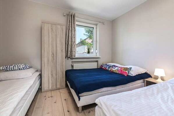 A bedroom with two beds, a window with curtains, a radiator, and a bedside lamp.