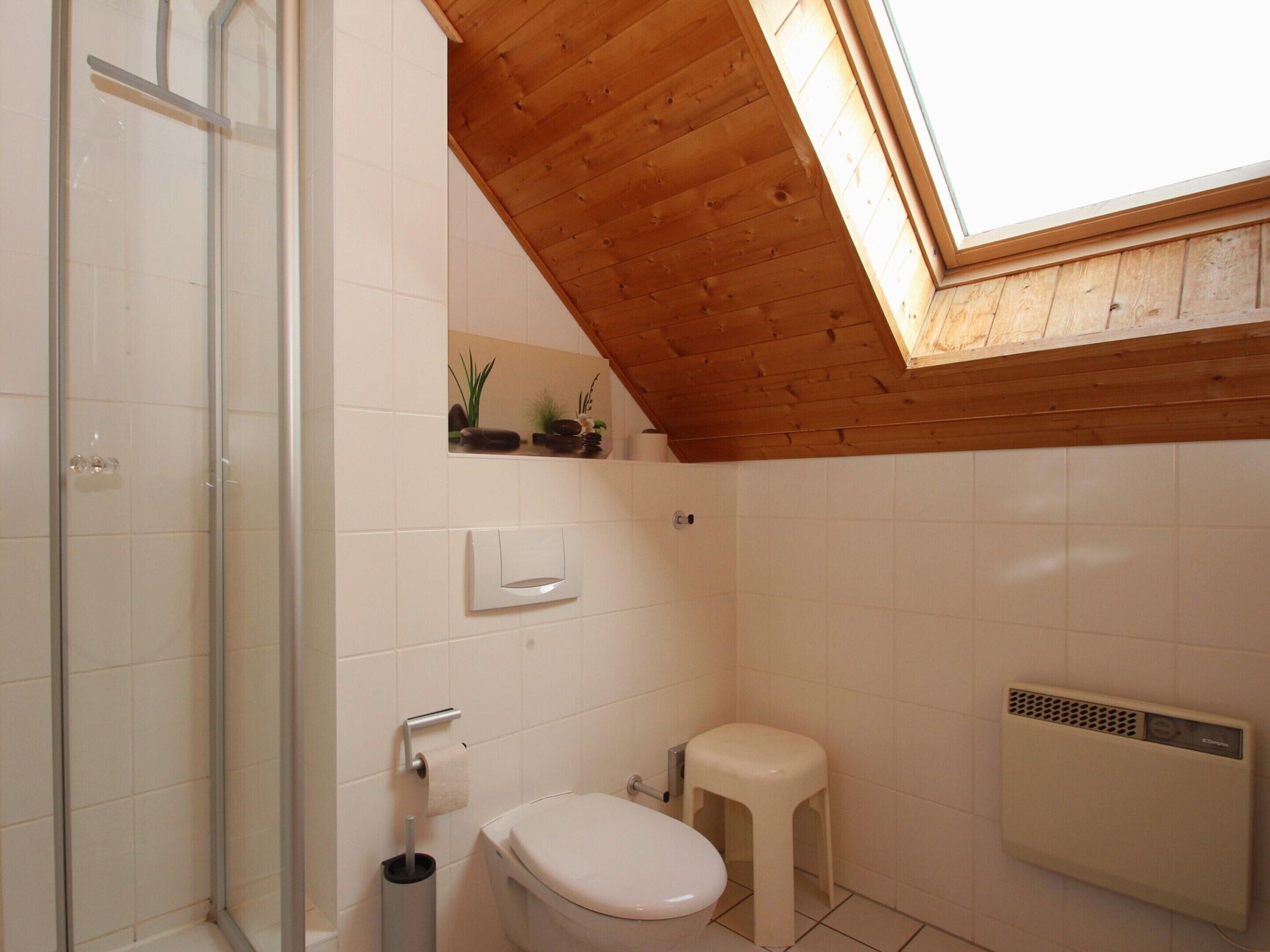 A bathroom with a skylight, a toilet, a small stool, and a radiator.