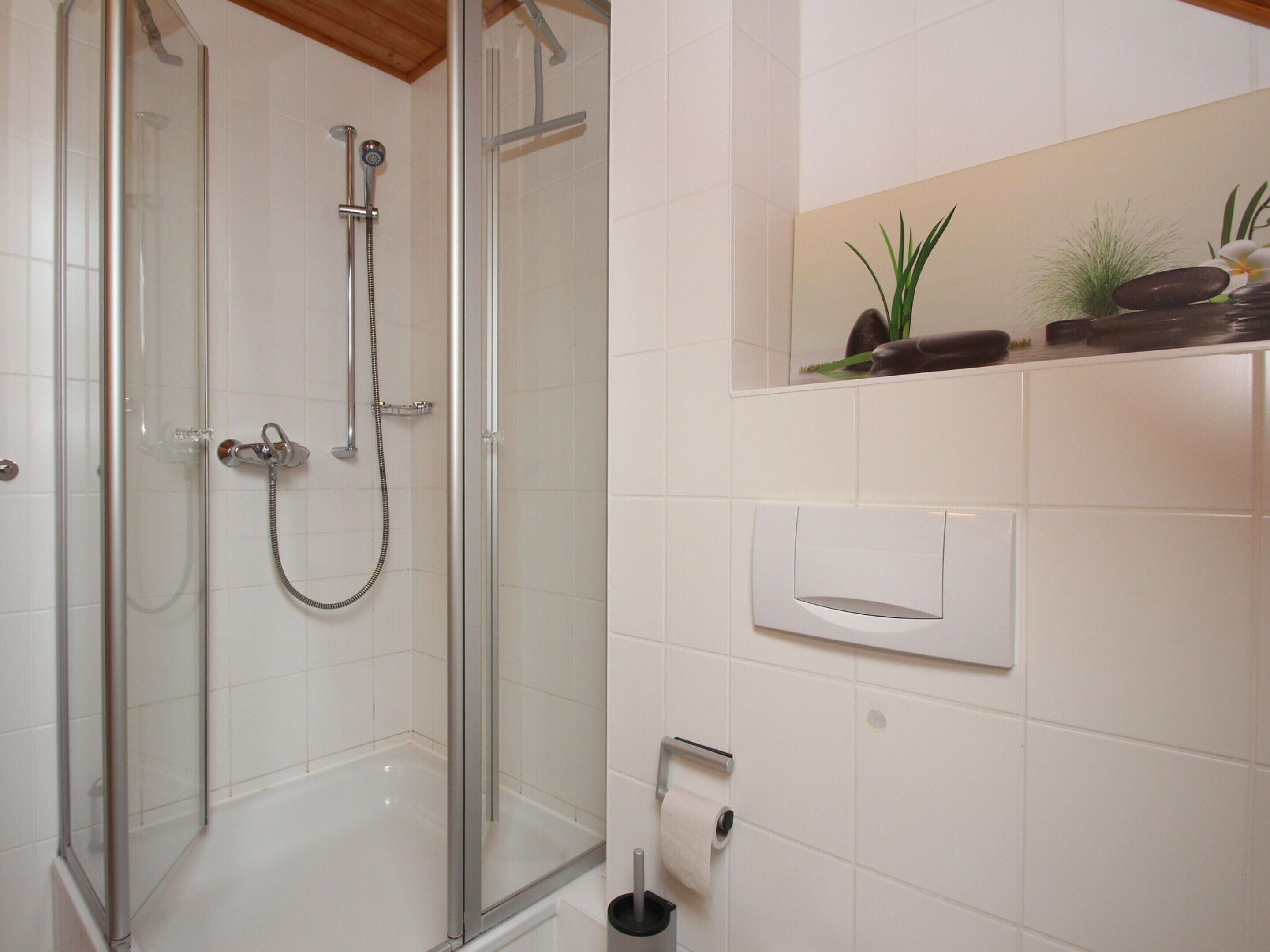 A shower with a glass door, a towel dispenser, and a toilet paper holder on the wall.