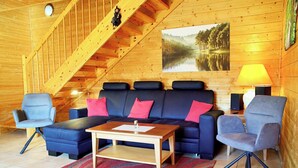 A wooden interior with a sofa, chairs, a coffee table, a lamp, a painting, and a staircase. - Doppelhaushalfte in Hasselfelde (Oberharz am Brocken)