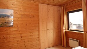 A wooden-paneled room with a bed, a window with curtains, and a radiator. - Doppelhaushalfte in Hasselfelde (Oberharz am Brocken)