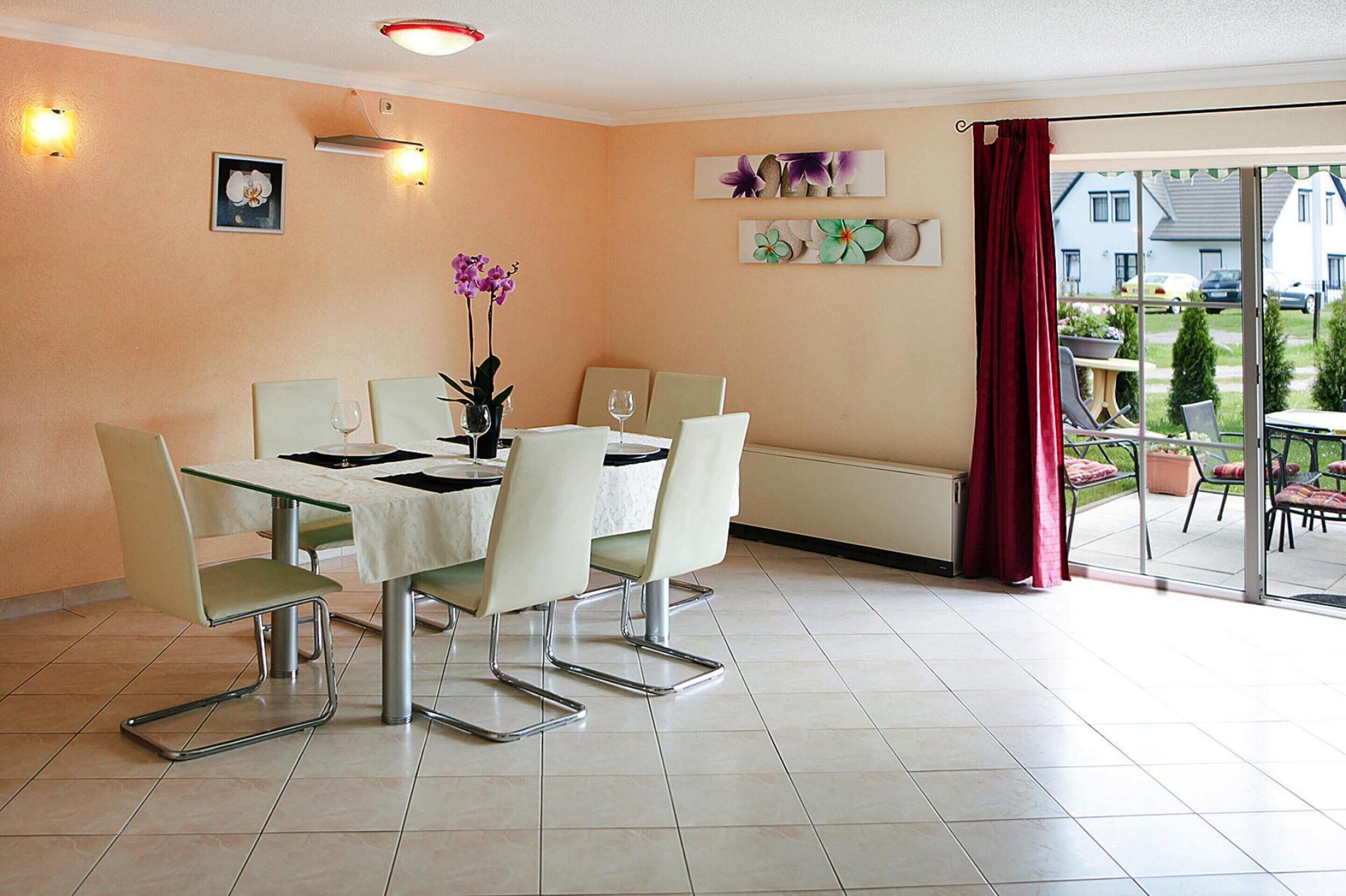A dining area with a table set for four, surrounded by chairs, and a view of the outside through a glass door.